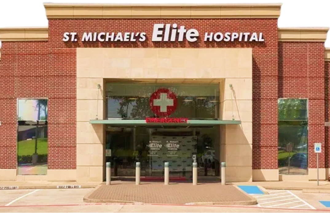 The exterior entrance of St. Michael’s Elite Hospital, featuring a brick building with modern glass doors and a paved walkway.