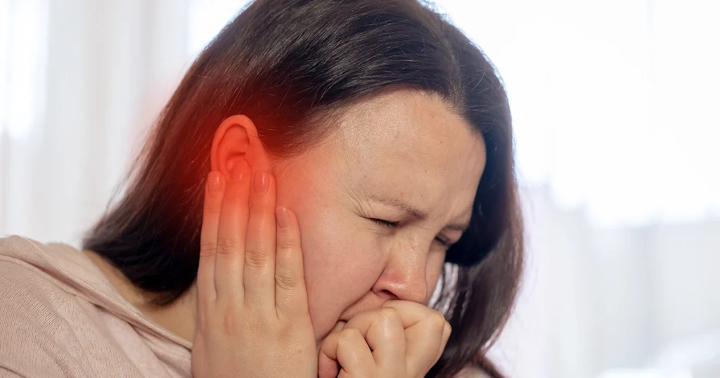 Woman holding ear, experiencing ear pain.