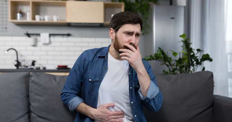 Man sitting on couch with stomach pain and nausea.