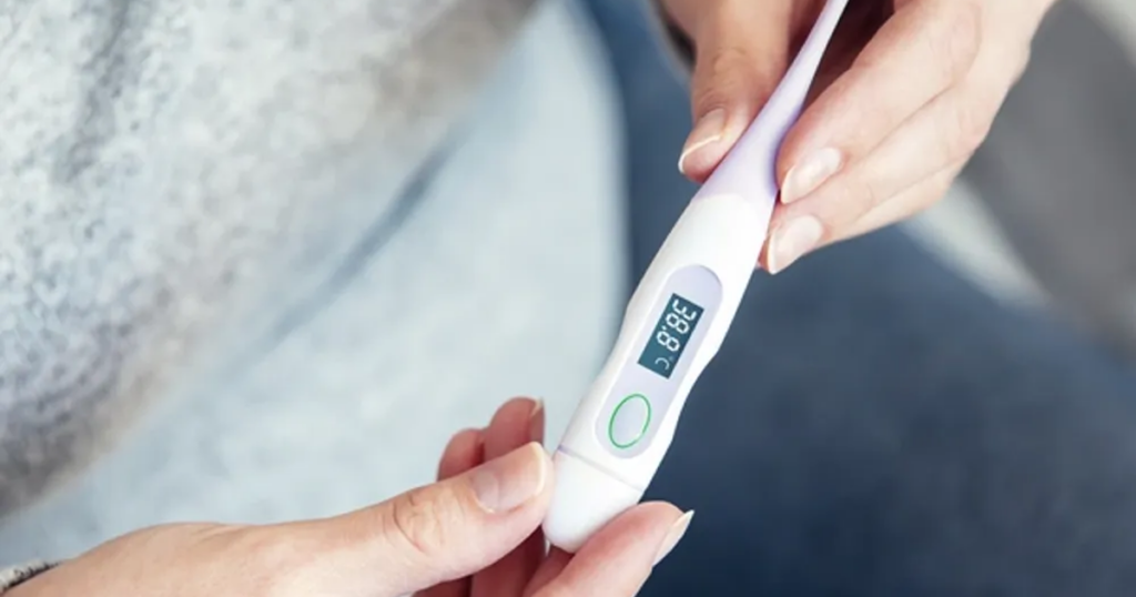 A close-up, high-definition photograph of a person’s hands holding a modern digital thermometer. The digital display clearly shows a temperature of 38.8°C, indicating a fever.