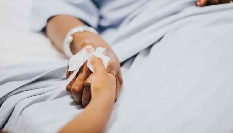 Loving hand holding a patient's hand with an IV catheter.